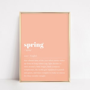 May include: A printable wall art print with a peach background and gold frame. The print features the word "spring" in white bold letters with a definition below. The definition reads: "that vibrant time of the year when nature wakes up from its long winter nap, light decides to stick around a little longer, birds compose symphonies, the world gets repainted in pastels and green, and trees conspire to make us sneeze for three months straight."