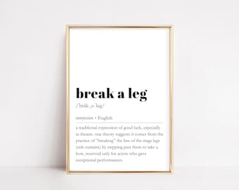 May include: A framed print with the phrase "break a leg" in bold black text. The definition of the phrase is below the text, along with the pronunciation and the word "interjection". The frame is gold.