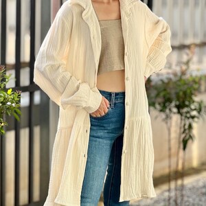 May include: A white, long-sleeved, button-down shirt with a ruffled hem. The shirt is made of a lightweight, textured fabric and has a relaxed fit.