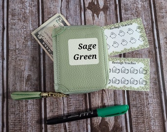 May include: Sage Green zippered wallet with a gold zipper pull and a green tassel. The wallet has a personalized name tag that says "Sage Green". The wallet is accompanied by two sheets of stickers with the text "Savings Tracker" and images of piggy banks and stacks of money.