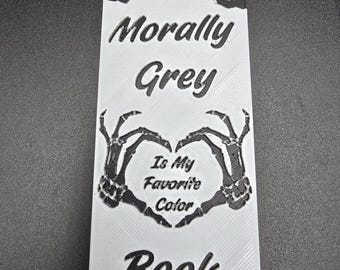 Könnte beinhalten: Weißes Lesezeichen mit schwarzem Text und schwarzem Band. Die Oberseite des Lesezeichens zeigt ein Blumendesign. Der Text lautet "Morally Grey", "Is My Favorite Color" und "Book Club". Ein Herz aus Skeletthänden befindet sich in der Mitte.