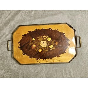 May include: A rectangular wooden serving tray with rounded corners and brass handles. The center features a dark brown wood inlay with a floral marquetry design in light yellow and tan, surrounded by a lighter, polished wood border with scrollwork.