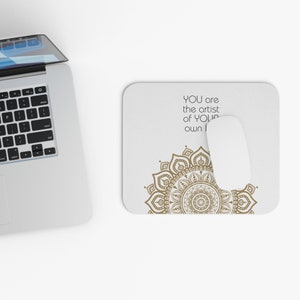 May include: A white mouse mat with a gold mandala design and the text "YOU are the artist of YOUR own life" in black.