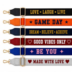 May include: Six adjustable bag straps with gold-tone metal swivel hooks and sliders. The straps feature various colors and text: black with LOVE LAUGH LIVE, orange with GAME DAY, navy with DREAM BELIEVE ACHIEVE, red with GOOD VIBES ONLY, blue with BE YOU, and light gray with MADE WITH LOVE.