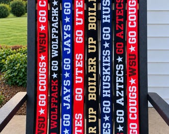 May include: Eight fabric bag straps in red, black, and blue with gold-tone swivel clasps. Each strap features white or gold text including WSU GO COUGS, GO WOLFPACK, GO JAYS, GO UTES, BOILER UP, GO HUSKIES, and GO AZTECS with star accents.