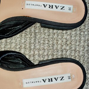 Puede incluir: Sandalias de tela negra con hebilla negra y una etiqueta blanca que dice "ZARA 38 TRAFALUC"