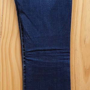 May include: A pair of dark blue denim jeans with a bootcut leg. The jeans have a red and white True Religion brand label on the back pocket.