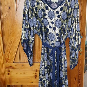 May include: A navy blue dress with gold sequins and a pattern of white and navy blue circles. The dress has long, wide sleeves and a matching navy blue belt. The dress is hanging on a floral patterned hanger.
