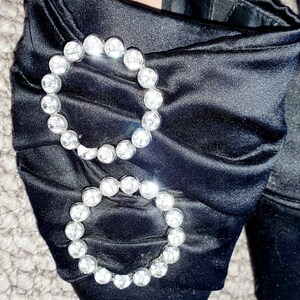 Puede incluir: Zapatos de tac&oacute;n de sat&eacute;n negro con punta puntiaguda y dos grandes adornos de pedrer&iacute;a. Los zapatos tienen una etiqueta que dice "TRAFA LUC" y "ZARA".