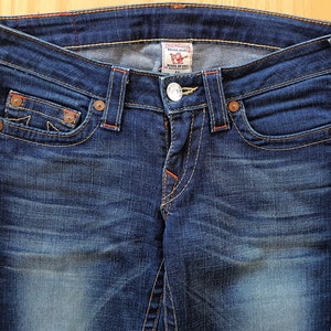 May include: A pair of blue denim jeans with orange stitching and a True Religion brand label. The jeans have a faded look and a classic five-pocket style.