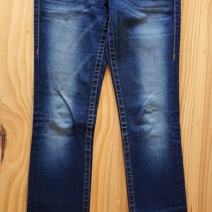 May include: A pair of dark blue denim jeans with a bootcut leg style. The jeans have a faded look and have a small brand label on the back waistband.