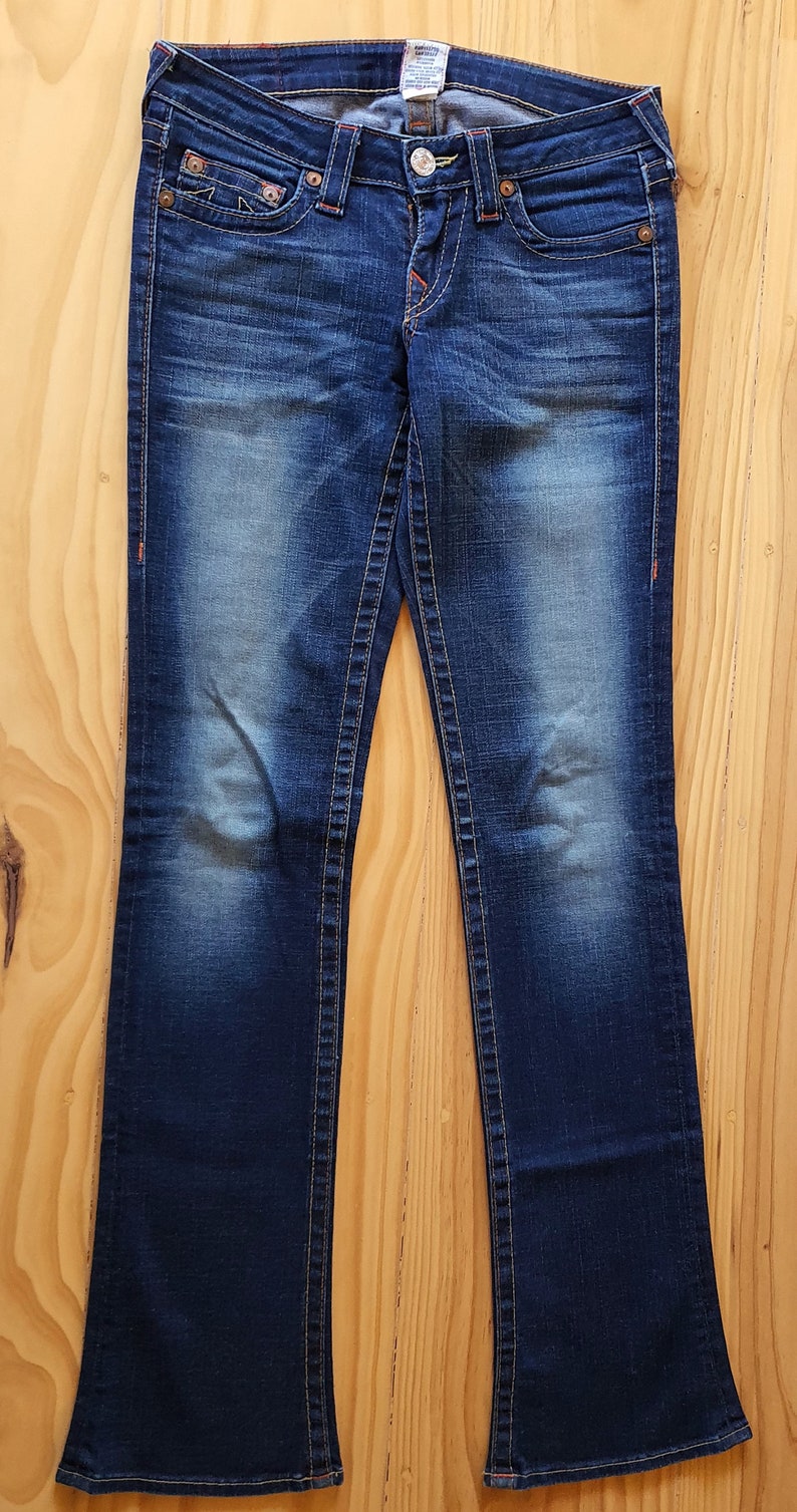 May include: A pair of dark blue denim jeans with a bootcut leg style. The jeans have a faded look and have a small brand label on the back waistband.