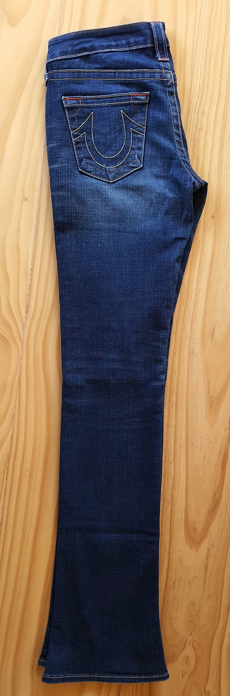 May include: A pair of dark blue denim jeans with a back pocket featuring a stitched-on True Religion logo.