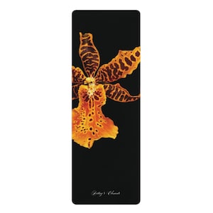 May include: A rectangular black yoga mat featuring a vibrant orange and dark brown orchid flower with spotted patterns on its petals. The text "Destiny's Elements" is printed in a small, elegant white script font near the bottom of the mat.