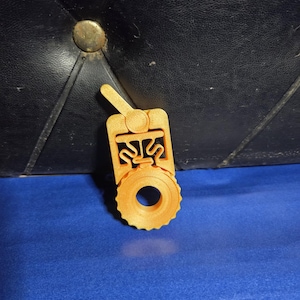 May include: A 3D-printed, orange-yellow object with a circular component and a handle. The object has a detailed, geometric design and appears to be a mechanical part or tool. It is set against a blue surface.