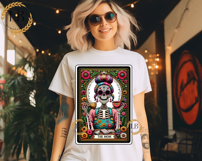 May include: A tarot card illustration featuring a skeleton wearing a colorful floral headdress and a blue and green apron. The card is titled "The Mom" and is surrounded by flowers and other decorative elements.