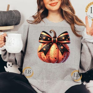 May include: A gray sweatshirt with a pumpkin design. The pumpkin is orange with black stars and a black and white bow. The bow has gold stars.