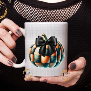 May include: White ceramic mug with a black and green pumpkin design. The pumpkin has a black bow and orange and green stripes.