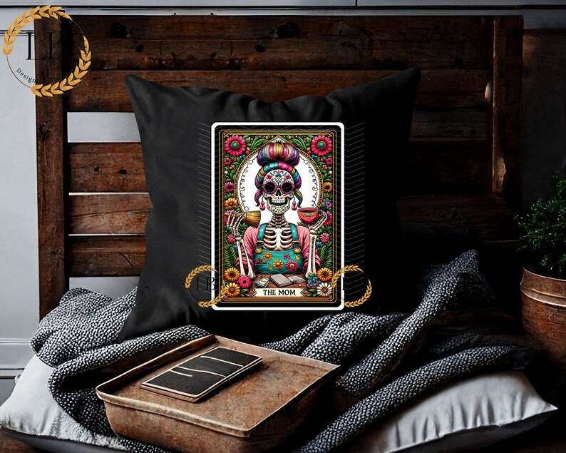 May include: A black throw pillow with a colorful illustration of a skeleton woman with a flower crown, holding a cup of coffee. The illustration is framed with a floral border and the text "The Mom" is at the bottom.