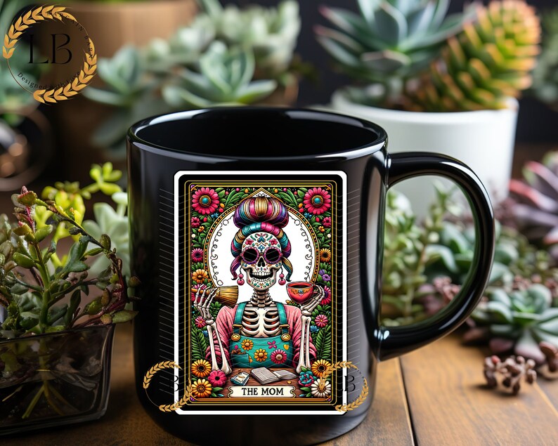 May include: Black coffee mug with a colorful illustration of a skeleton woman with a floral background. The illustration is in the style of a tarot card and says "The Mom" at the bottom.
