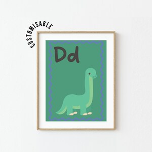 May include: A framed wall art print featuring a green background with a dark blue scalloped border. The letter Dd is printed in black at the top, and a light green cartoon dinosaur is centered below. The word CUSTOMISABLE is arched above the frame.