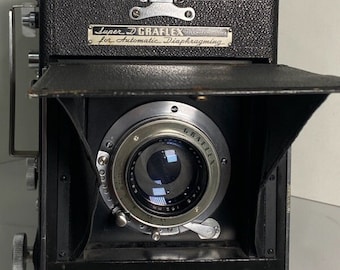 Może przedstawiać: Czarny aparat Super D Graflex z srebrnym obiektywem i czarnym mieszkiem. Aparat ma etykietę z napisem "Super D Graflex for Automatic Diaphragming".