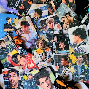 Pode incluir: Uma coleção de cartões retangulares brilhantes com imagens de pilotos de Fórmula 1. Os cartões mostram vários pilotos com seus trajes de corrida, com logotipos de equipes e marcas de patrocinadores. Alguns cartões têm detalhes de glitter em forma de estrela.