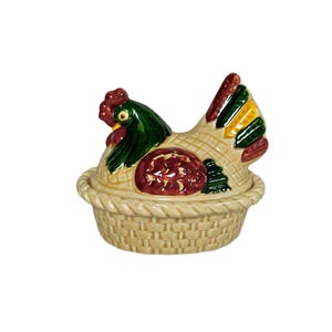 May include: A ceramic chicken shaped butter dish with a woven basket design. The chicken is painted with green, red, and yellow accents.