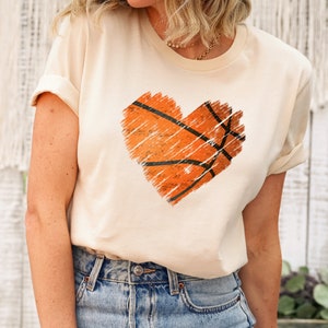 May include: A cream coloured t-shirt with a distressed orange basketball graphic in the shape of a heart.