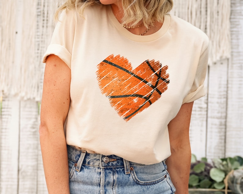 May include: A cream coloured t-shirt with a distressed orange basketball graphic in the shape of a heart.