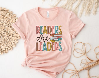 May include: Pink t-shirt with the text "Readers are Leaders" in colorful letters with a stack of books in the middle of the text.