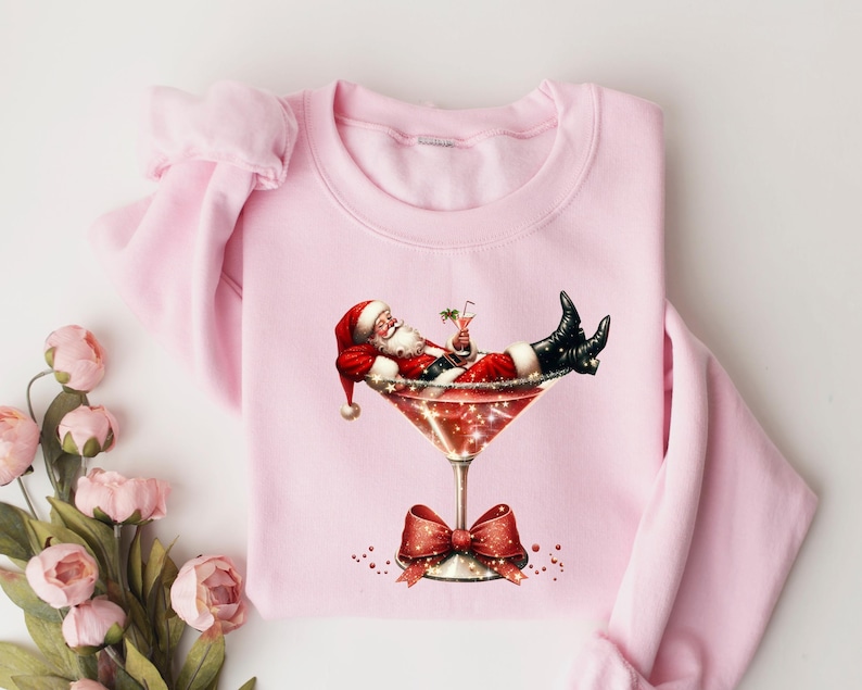 May include: Pink Christmas sweatshirt with a graphic of Santa Claus relaxing in a martini glass.