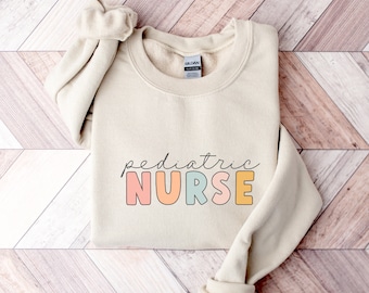 May include: A beige sweatshirt with the text "pediatric NURSE" in rainbow colors. The letters are outlined in black.