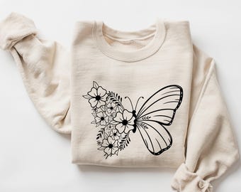 May include: A cream-colored sweatshirt with a black butterfly and floral design. The butterfly is flying towards the right and has a floral design on the left side of its body.