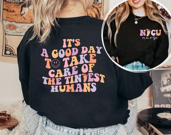 Puede incluir: Camiseta negra de manga larga con un gráfico de fuente retro colorido que dice "It's a good day to take care of the tiniest humans". La camiseta también presenta un pequeño gráfico de cara sonriente. La parte posterior de la camiseta tiene un gráfico en blanco y negro que dice "NICU nurse".
