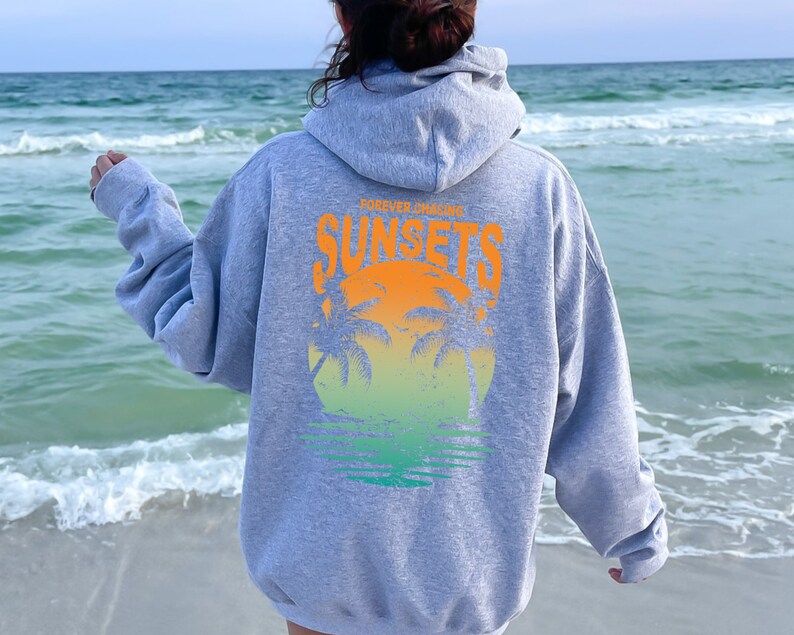 May include: Gray hooded sweatshirt with a graphic print of a sunset and palm trees. The text "FOREVER CHASING SUNSETS" is printed on the sweatshirt.