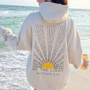 May include: A white hoodie with a black sunburst design and the text "BE THE LIGHT" and "MATTHEW 5:14" on the back.