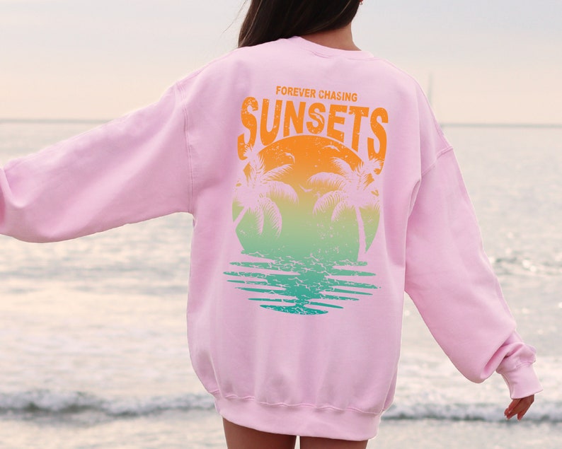 May include: Pink sweatshirt with a graphic print of palm trees and a sunset. The text "FOREVER CHASING SUNSETS" is printed on the sweatshirt.