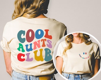 May include: Two women wearing cream colored t-shirts with the text "Cool Aunts Club" in rainbow colors. The text is in a retro font style. One shirt has the text on the back and the other has the text on the front with a smiley face made of two red dots.