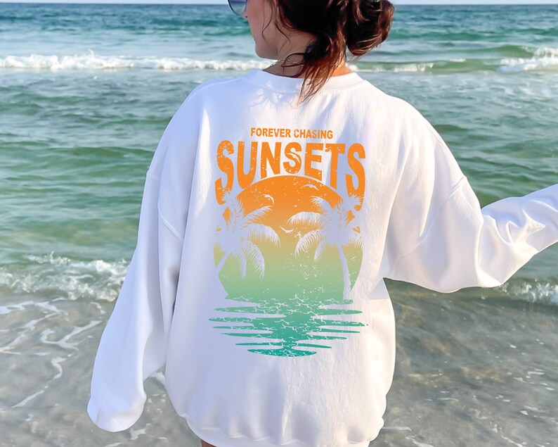 May include: White sweatshirt with a graphic print of a sunset with palm trees and the text "FOREVER CHASING SUNSETS".