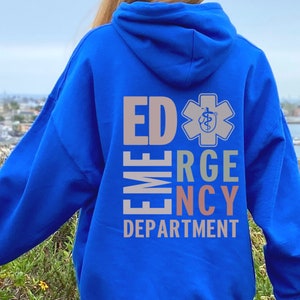 May include: A royal blue hooded sweatshirt with the text "ED", "EME", "RG", "NCY", and "DEPARTMENT" in a vertical column. The text is in a rainbow of colors. A white star with a medical symbol is above the text.