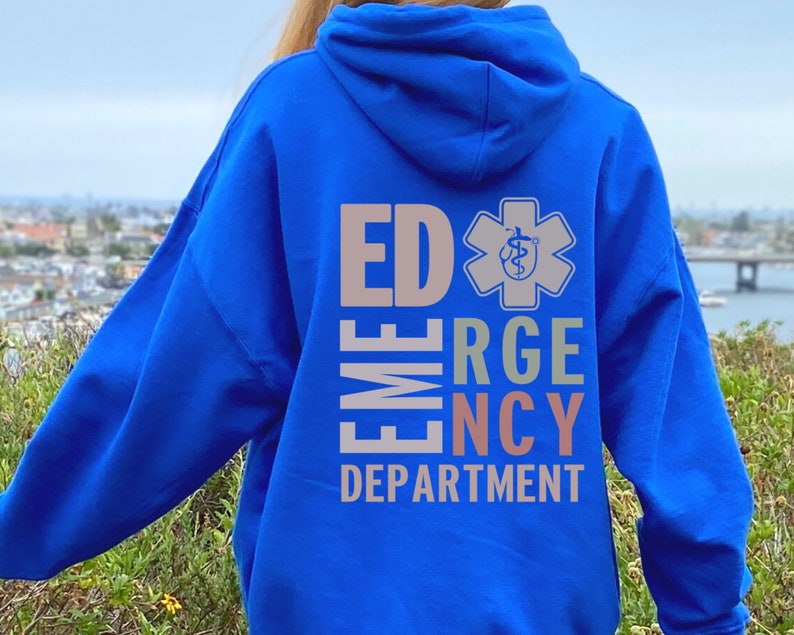 May include: A royal blue hooded sweatshirt with the text "ED", "EME", "RG", "NCY", and "DEPARTMENT" in a vertical column. The text is in a rainbow of colors. A white star with a medical symbol is above the text.
