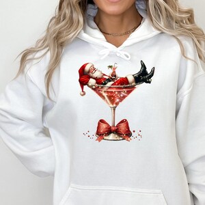 May include: White hooded sweatshirt with a graphic of Santa Claus relaxing in a martini glass with a red bow on the stem.