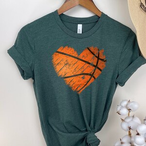 May include: A dark green t-shirt featuring a distressed orange basketball design in the shape of a heart.
