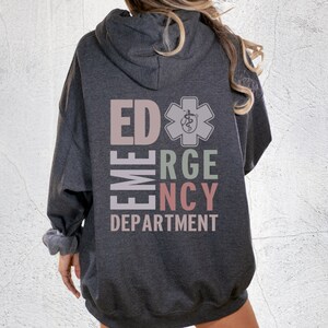 May include: A dark grey hooded sweatshirt with the text "ED EMERGENCY DEPARTMENT" in a vertical column with a medical symbol in the center. The text is in different colors, including pink, green, and light brown.