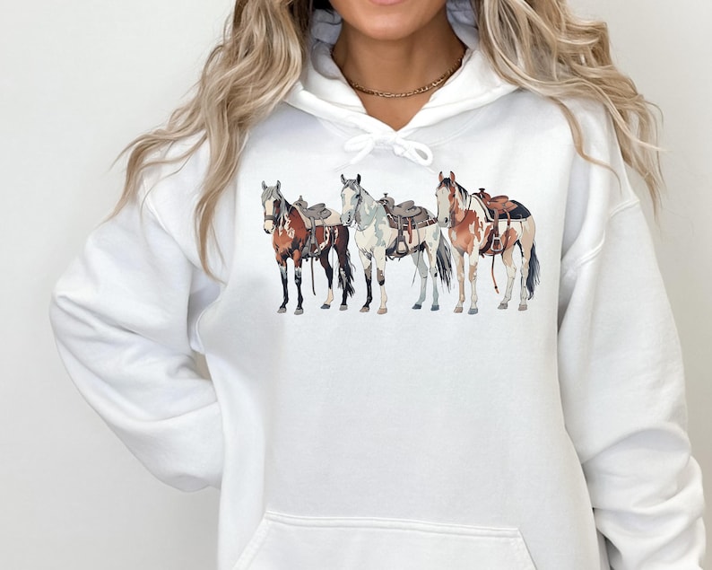 May include: White hoodie with a graphic of four horses wearing saddles. The horses are brown, white, and black.