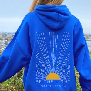 May include: A royal blue hoodie with a white sunburst design and the text "BE THE LIGHT" and "MATTHEW 5:14" in white.