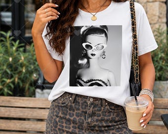 May include: A white short-sleeve t-shirt featuring a black and white graphic print of a doll wearing cat-eye sunglasses and earrings. The t-shirt is paired with a brown and black leopard print denim mini skirt with a frayed hemline.