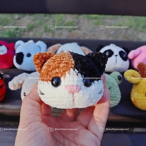 May include: A collection of crocheted stuffed animal keyrings, including a red panda, a blue koala, a brown and black cat, a black and white panda, a pink bird, a green frog, and a yellow giraffe.