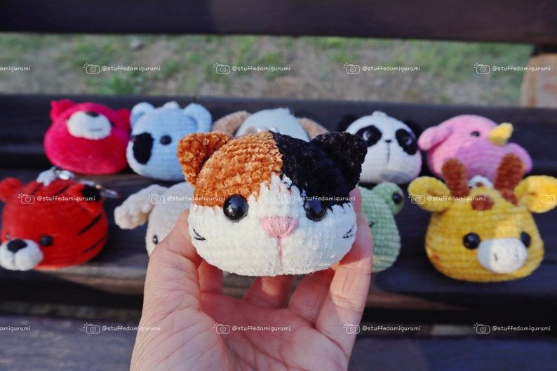 May include: A collection of crocheted stuffed animal keyrings, including a red panda, a blue koala, a brown and black cat, a black and white panda, a pink bird, a green frog, and a yellow giraffe.